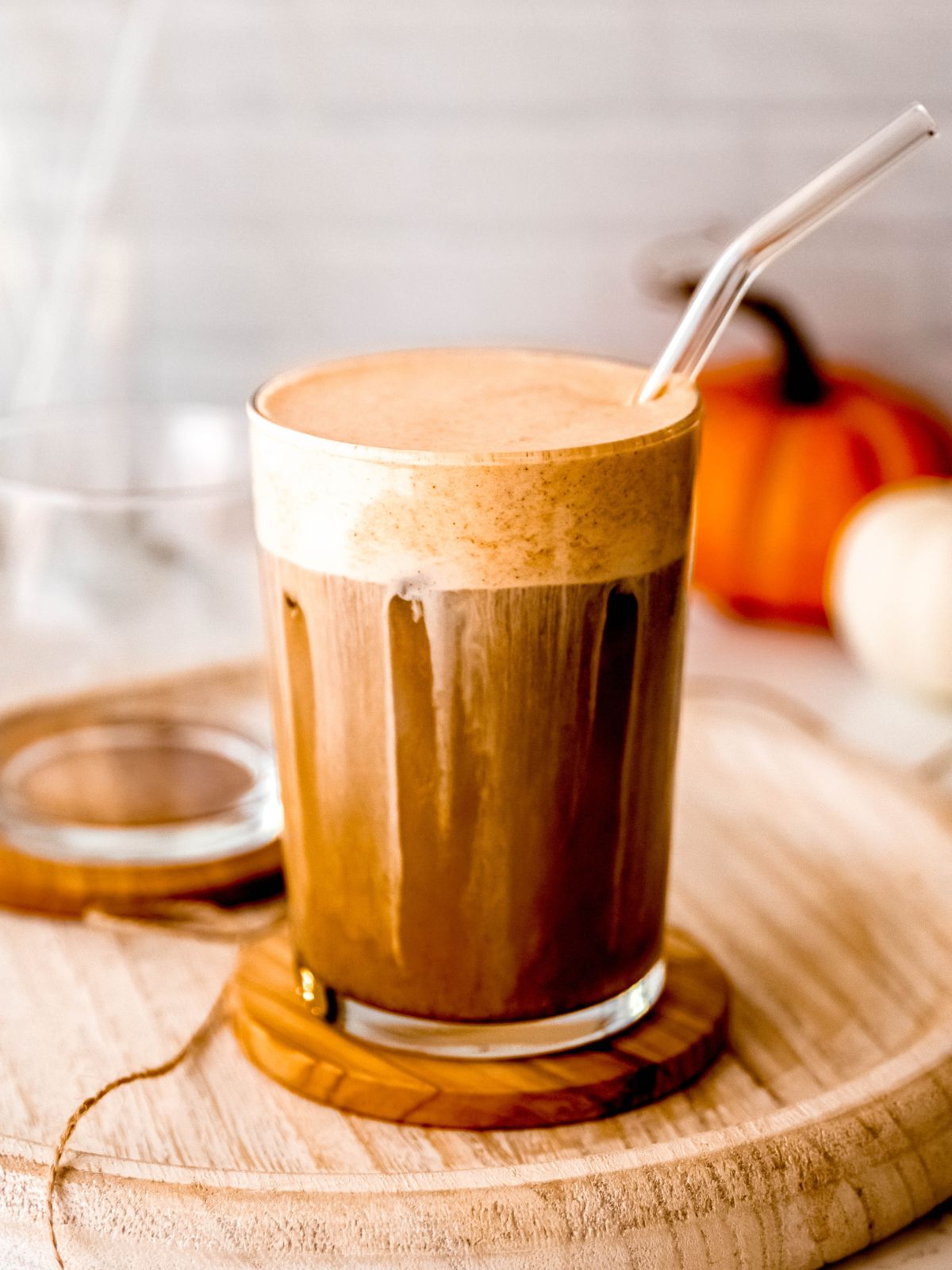 A glass of pumpkin latte on a wooden board with a straw.