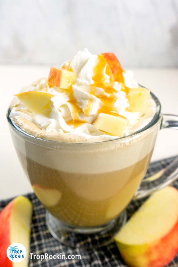 A cup of apple latte with whipped cream and apple slices.