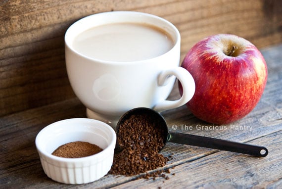 A cup of coffee with an apple and cinnamon next to it.