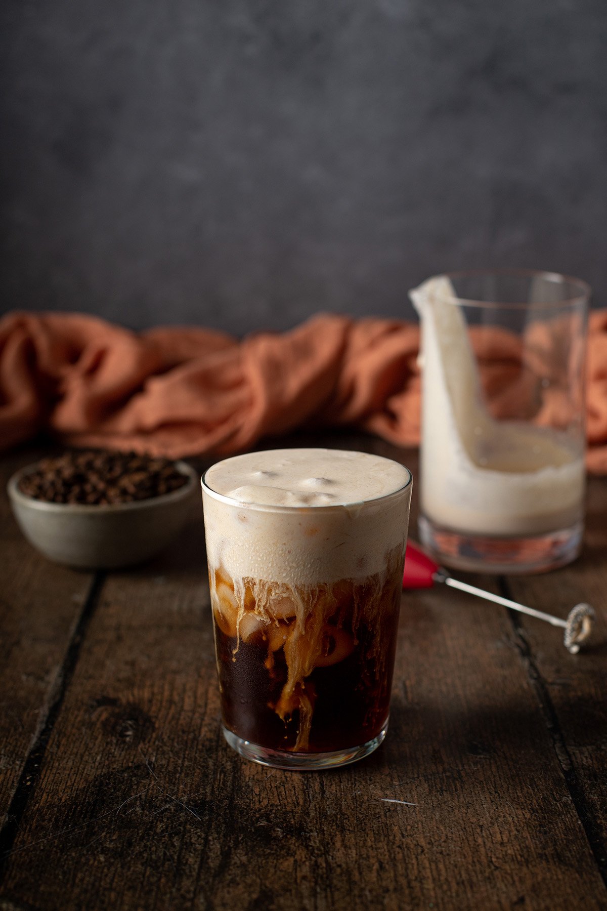 An iced coffee with whipped cream and coffee beans on a wooden table.