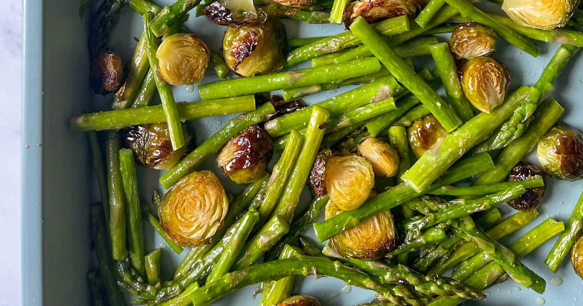 Roasted asparagus and brussel sprouts on a baking sheet.