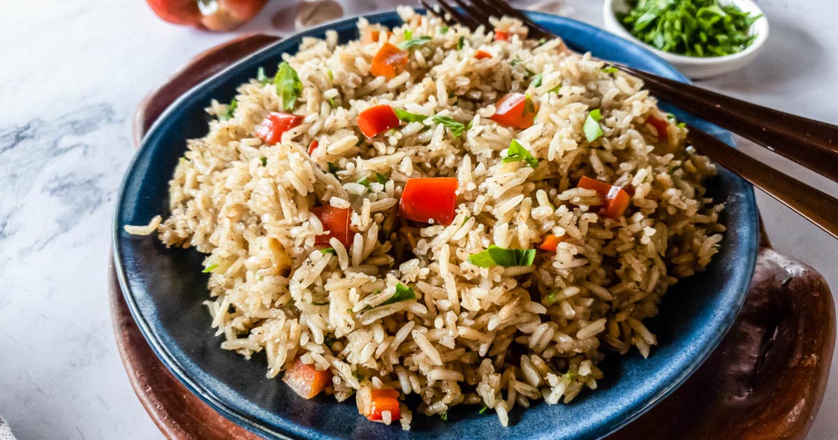 A bowl of rice pilaf with vegetables and fresh parsley garnish.