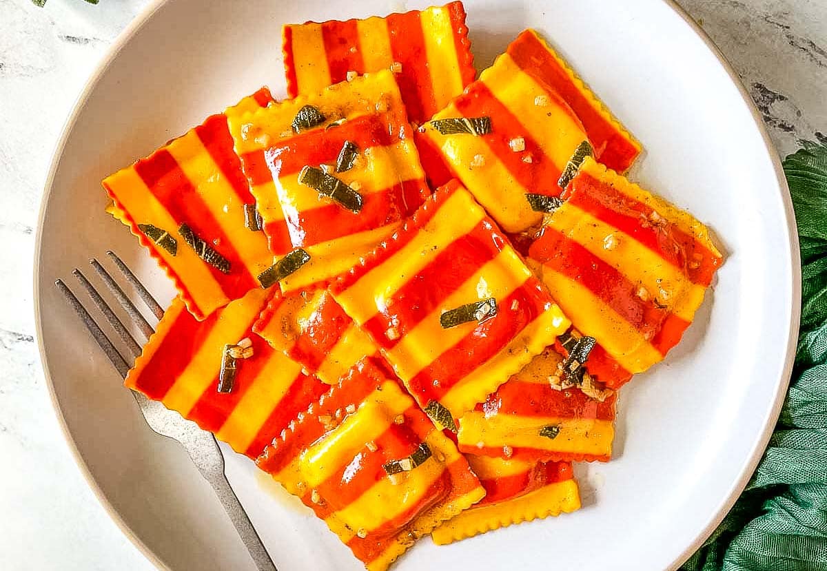 Orange and yellow lobster ravioli on a white plate with a fork.