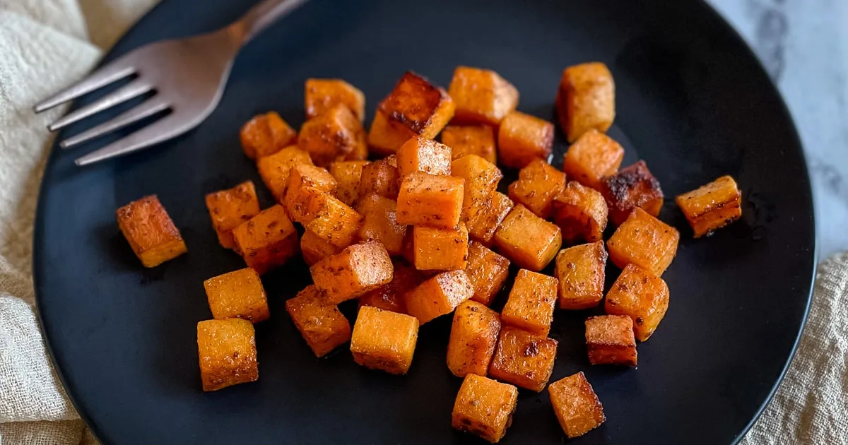 Roasted sweet potato cubes on a black plate.
