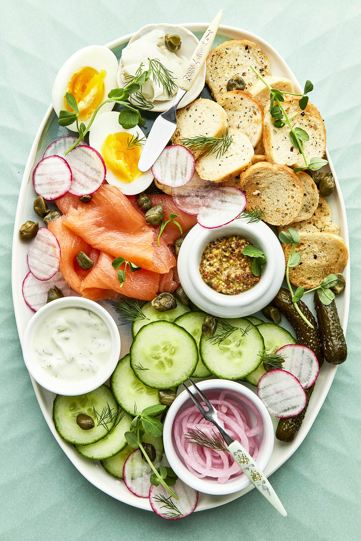 A plate with smoked salmon, cucumbers, eggs and bread.