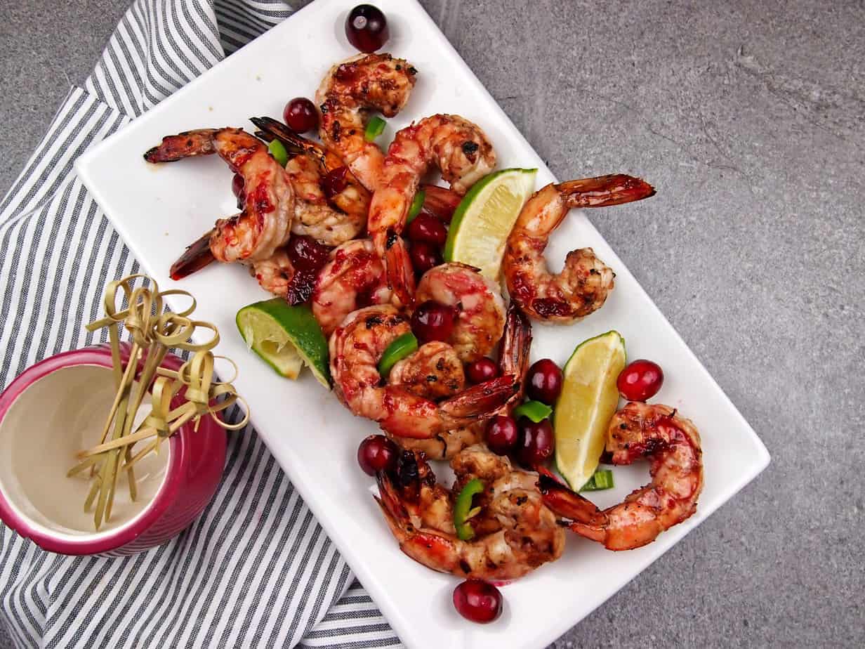 Grilled shrimp with cranberries and limes on a white plate.