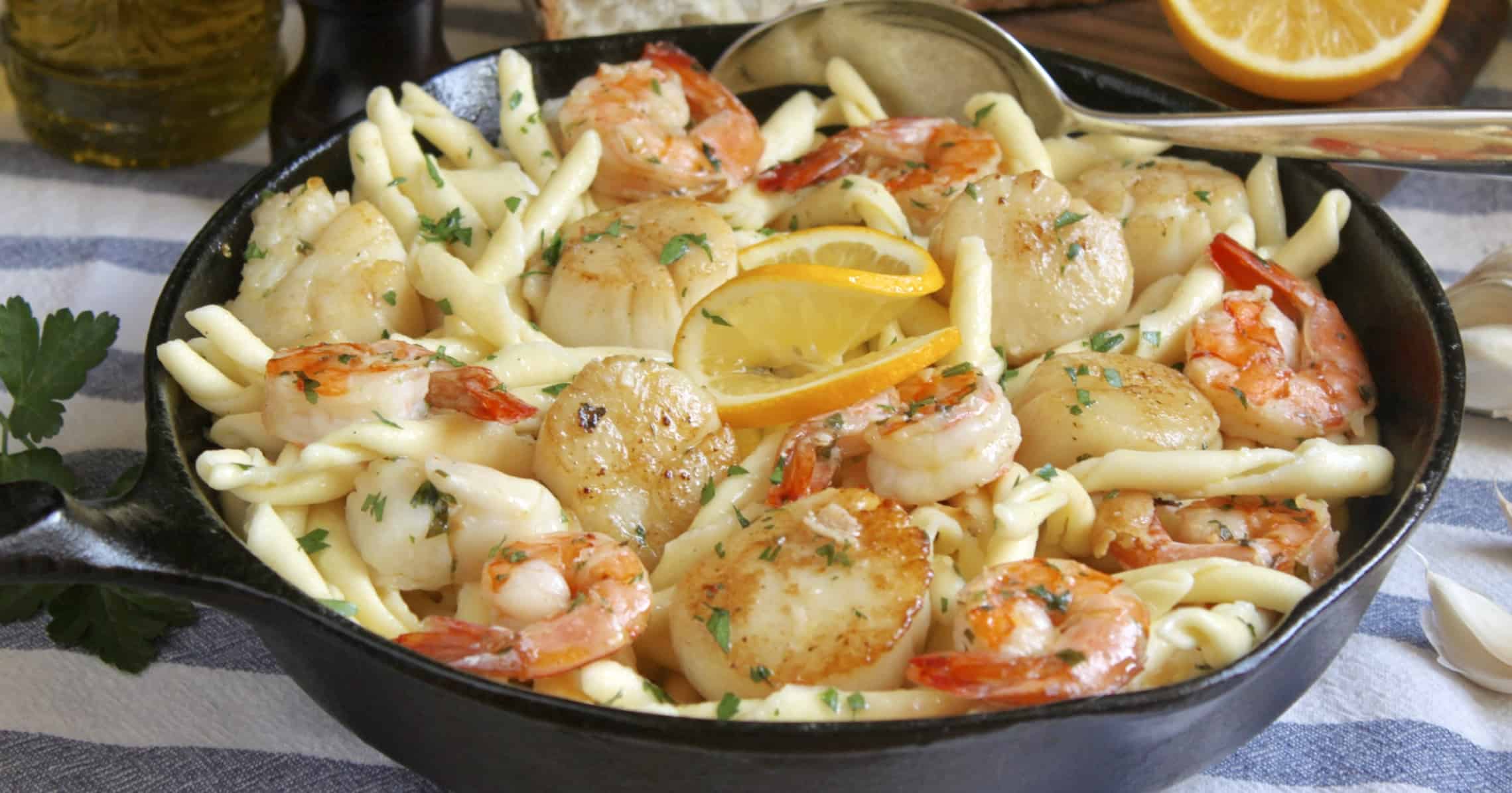 A skillet filled with pasta, shrimp and lemons.