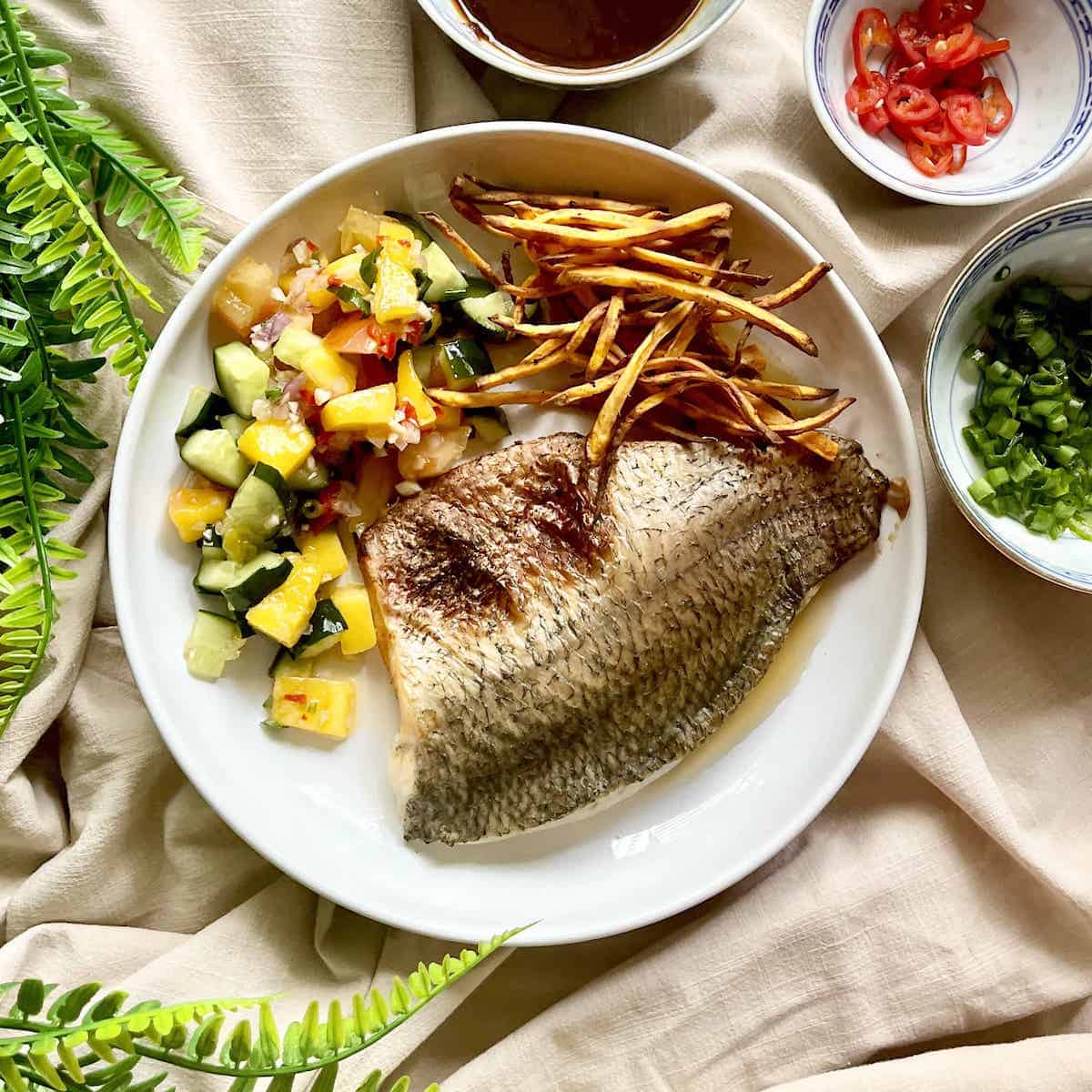 A plate with miso sea bass, fries and vegetables on it.