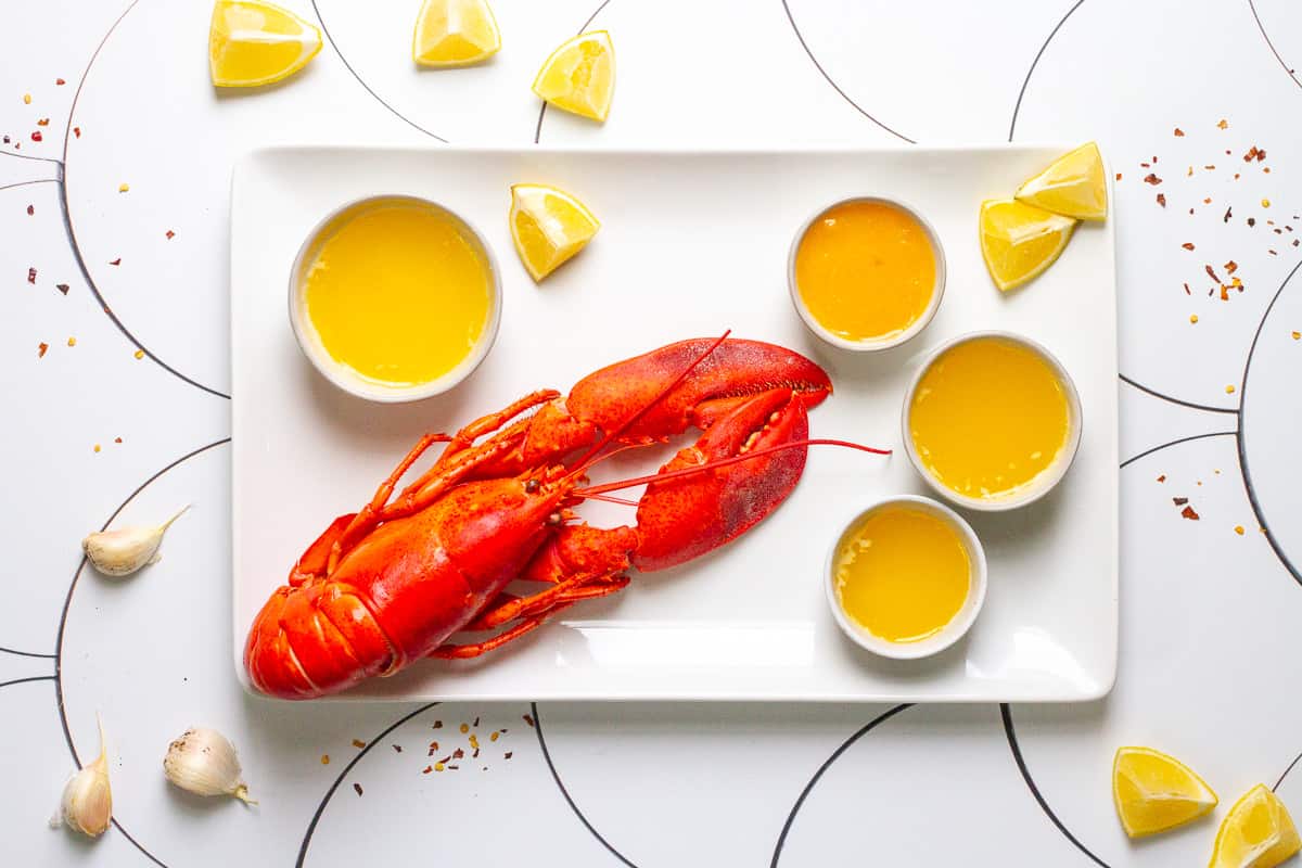 A lobster on a white plate with with butter sauce, lemons and garlic.