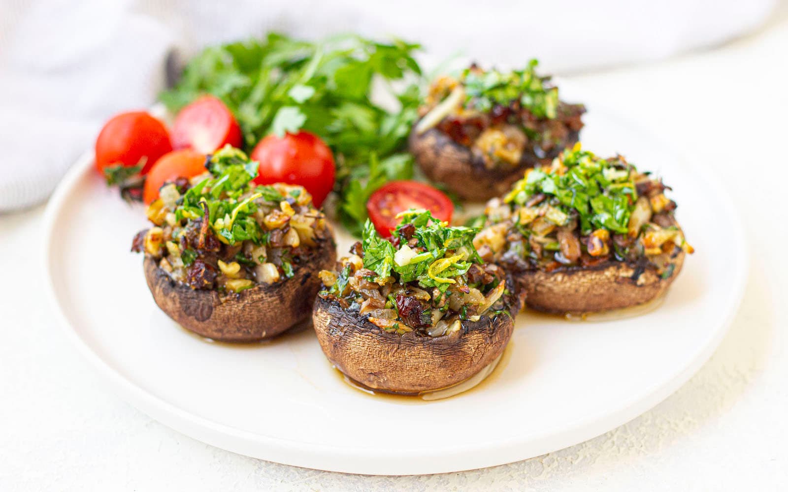 Four stuffed mushrooms with vegetablles on the side on a white plate.