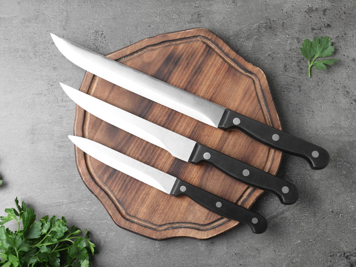 Three knives on a wooden cutting board with parsley.