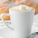 A white cup of cappuccino with whipped cream on a saucer.