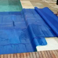 A man laying down a blue pool cover on a wooden deck.