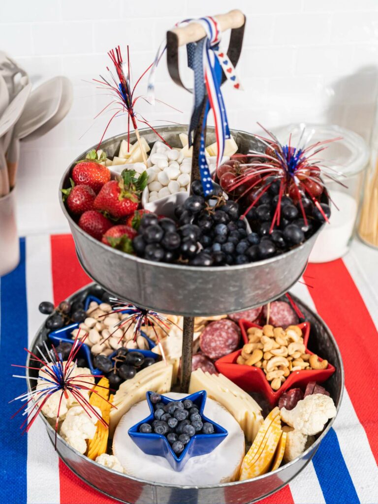 A three-tiered serving tray filled with a variety of snacks and decorated in a patriotic theme with red, white, and blue accents.