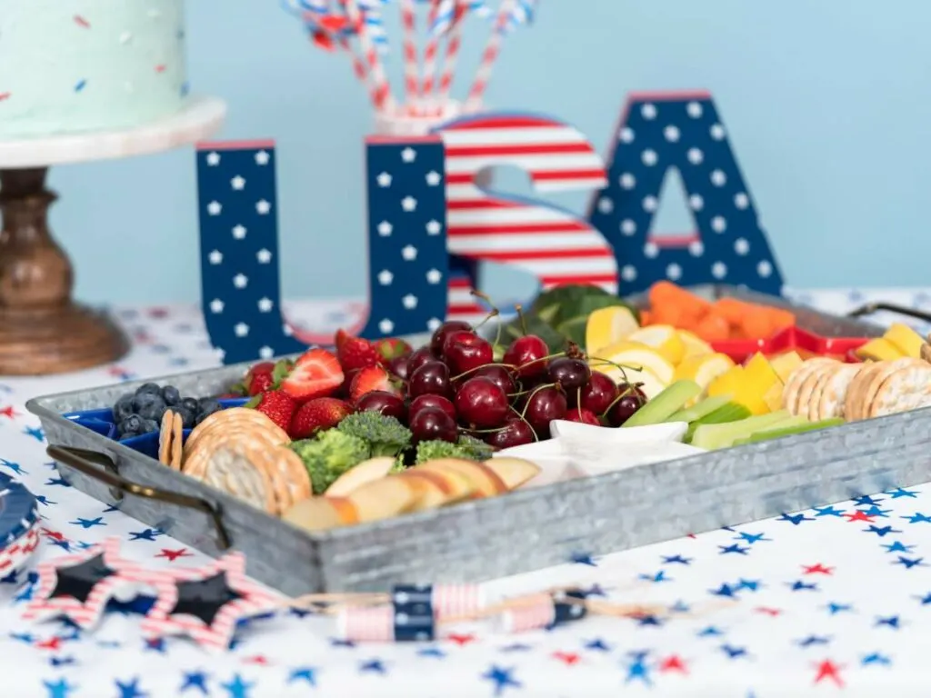 A vibrant display of fruit arranged in a tray at a patriotic-themed event with decorative "usa" letters in the background.