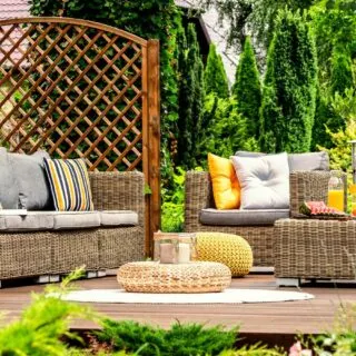 A cozy outdoor seating area featuring wicker furniture with cushions, a rug, and surrounded.