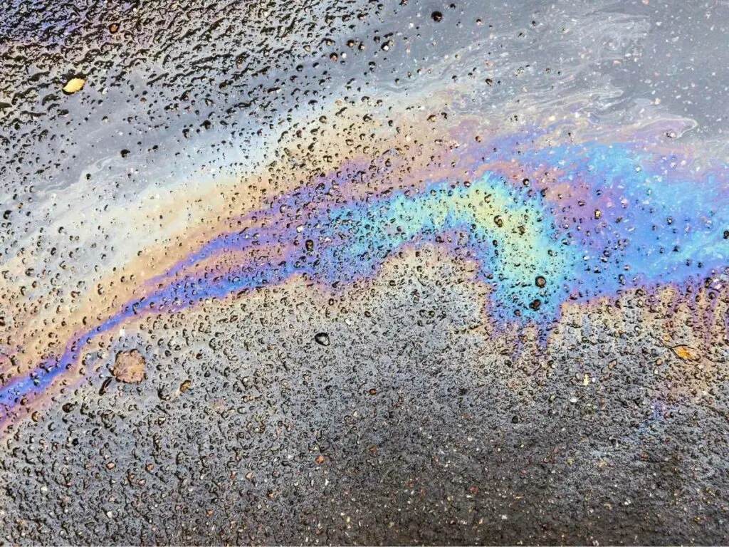 Oil slick on a wet, pebbled pavement creating a rainbow-like sheen.