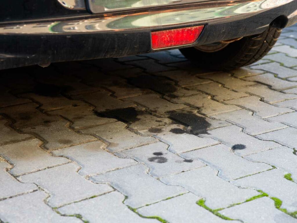 Oil stains on a patterned brick driveway beneath a parked car.
