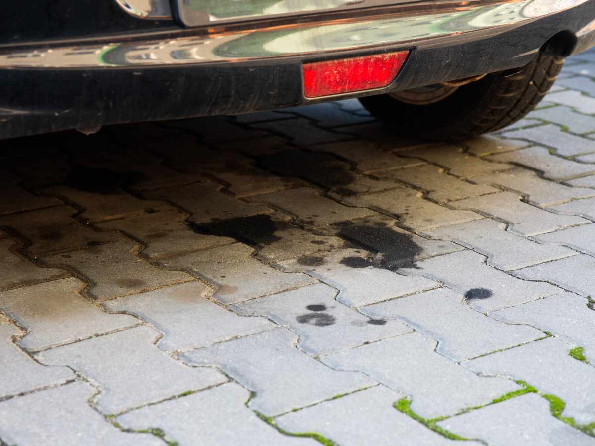 Oil stains on a patterned brick driveway beneath a parked car.