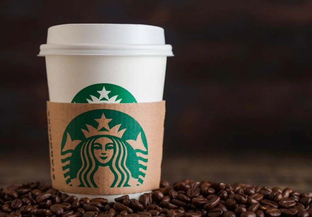 A starbucks coffee cup with a logo sleeve, placed on a surface scattered with coffee beans, against a dark wooden background.