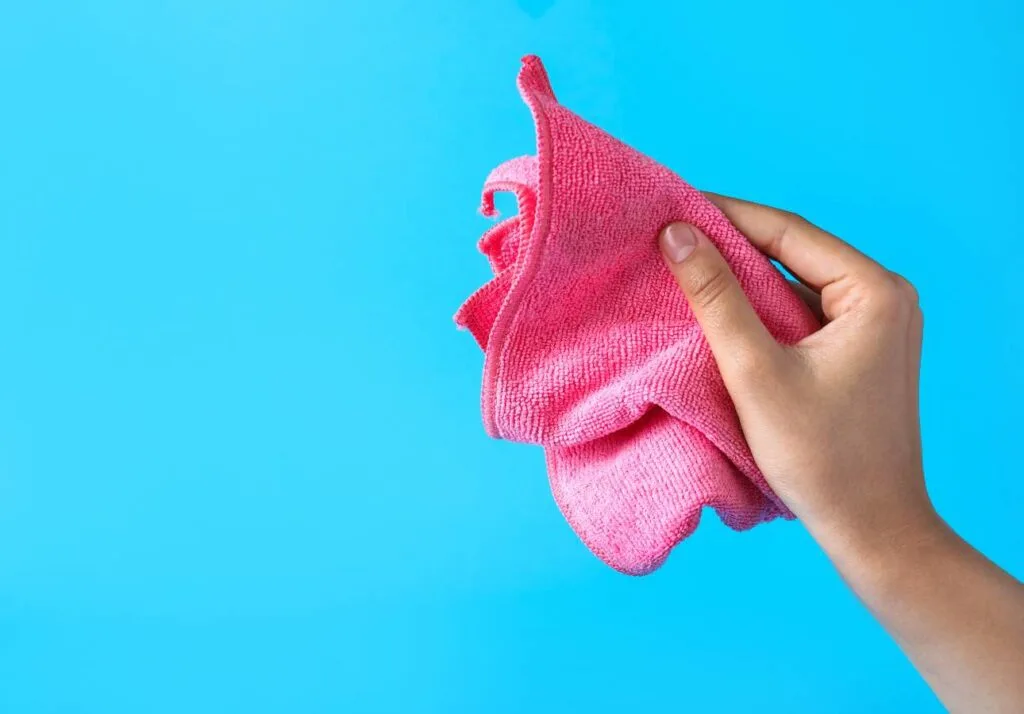 A hand holding a pink cleaning cloth against a blue background.