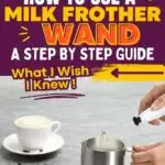 A person uses a milk frother wand in a metal pitcher, with a cup of coffee and scattered coffee beans on a gray surface. Text: "How to Use a Milk Frother Wand - A Step by Step Guide. What I Wish I Knew!.