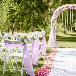 Outdoor wedding ceremony setup with white folding chairs draped in a garden setting.