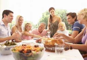 Family and friends gathered around a table enjoying a meal together outdoors.