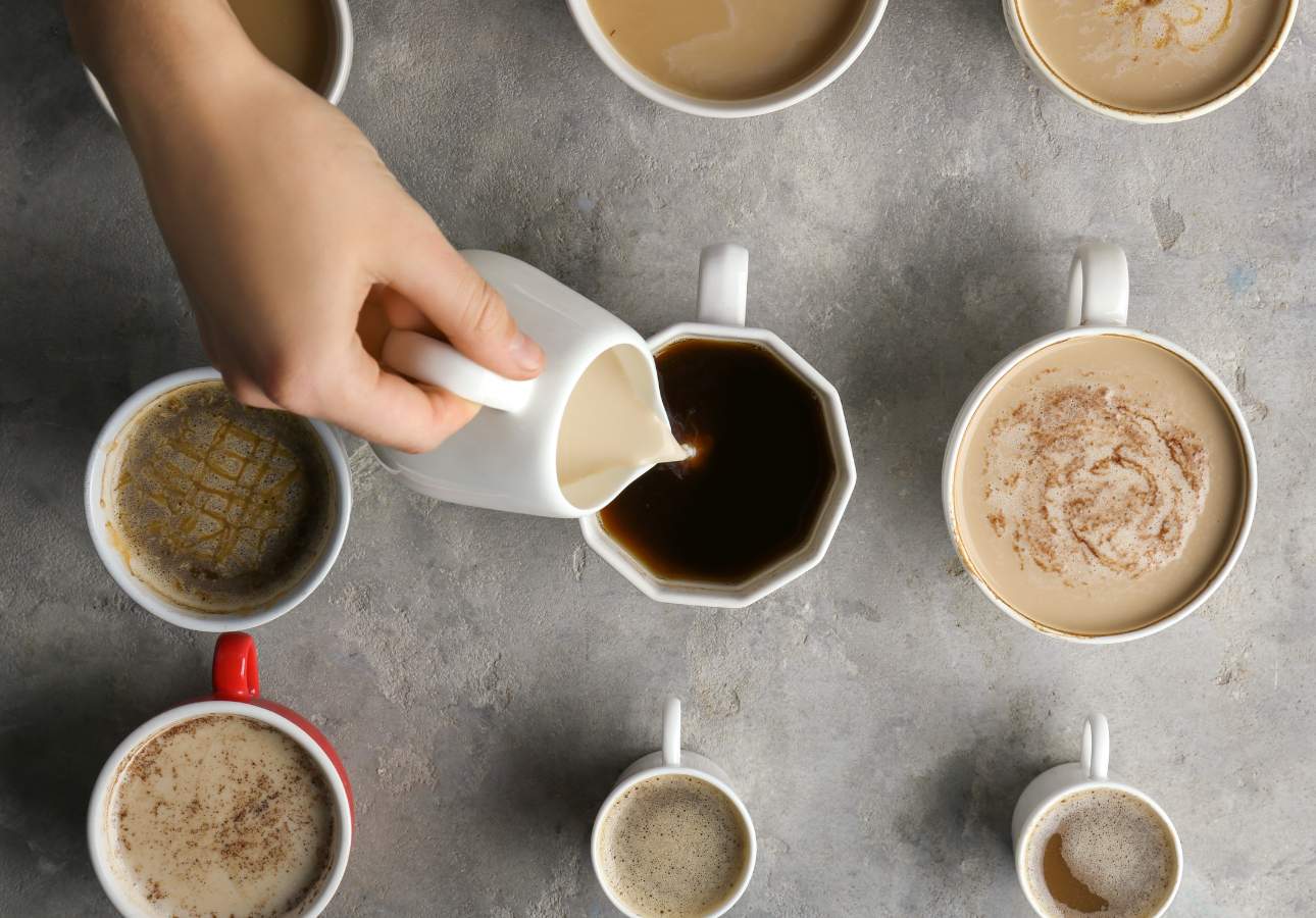 A person pouring coffee into cups, each containing different amounts of milk.