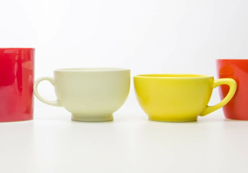 Four colorful cups of various shapes and sizes lined up on a white surface; two red, one white, and one yellow.