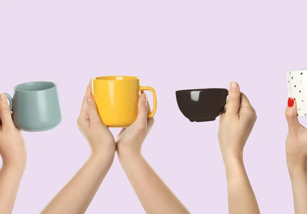 Four hands holding different colored mugs against a purple background: pale blue, yellow, black, and white with polka dots.