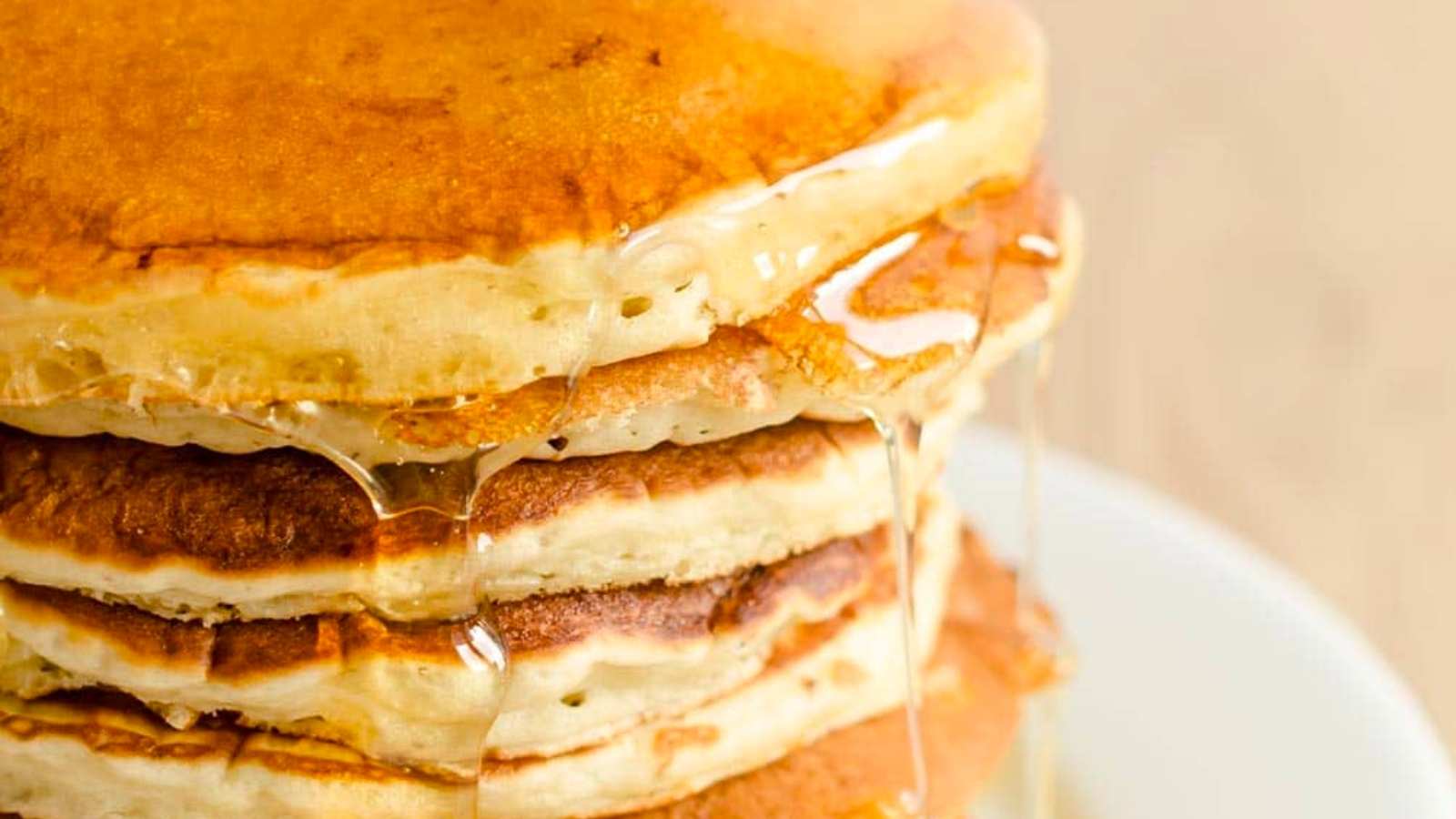 A close-up of a stack of golden-brown pancakes drizzled with syrup.