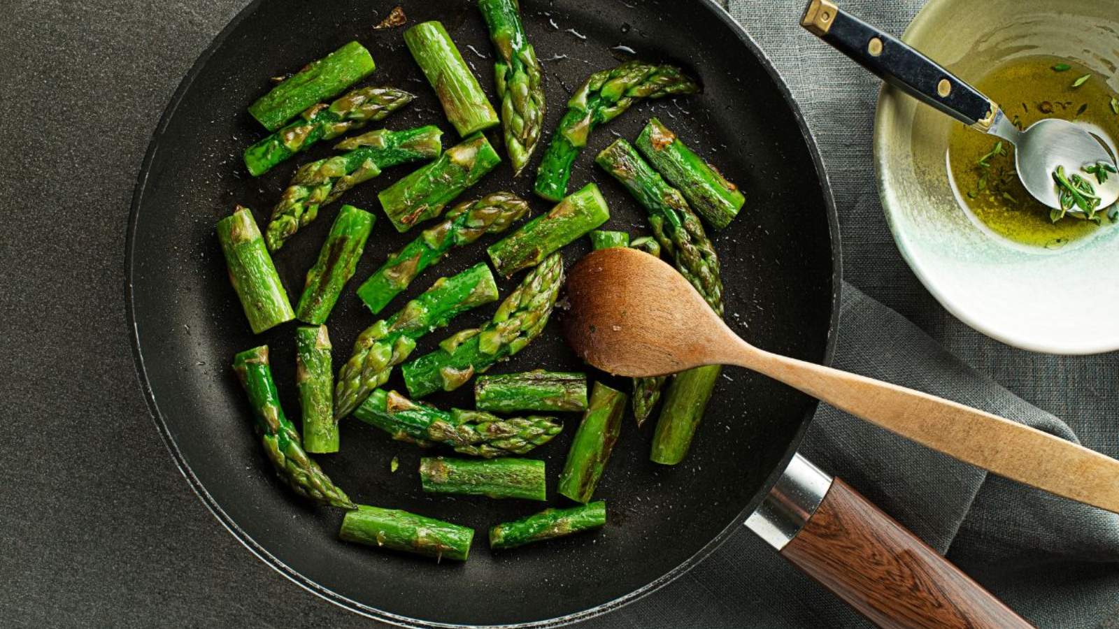 A skillet with sautéed asparagus spears, stirred with a wooden spoon.