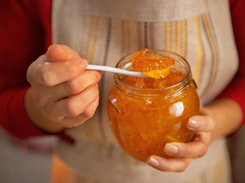 A person in an apron holds a jar of marmalade.