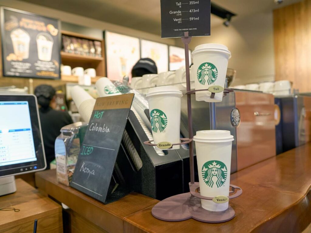 Display of various Starbucks cup sizes on a stand at a Starbucks counter.