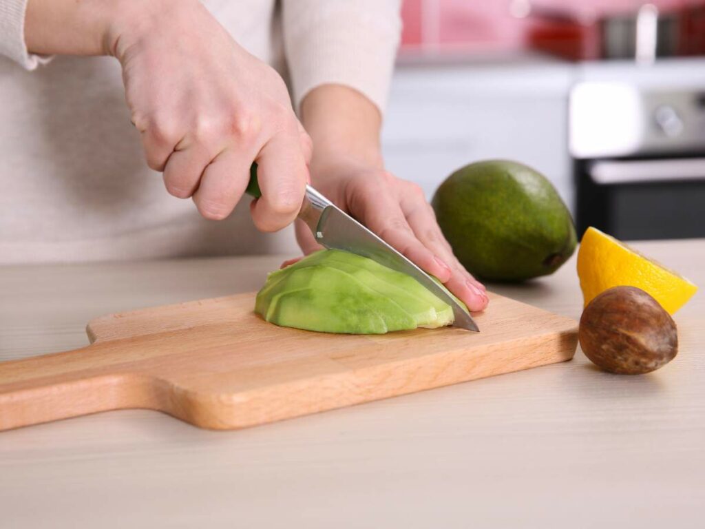 Close-up of hands slicing an avocado on a wooden cutting board.