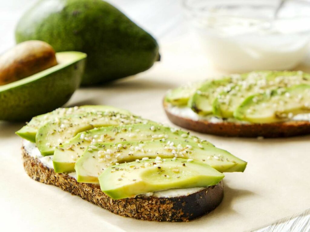 Sliced avocado on toast with a sprinkle of seeds, placed on a sheet of parchment paper.