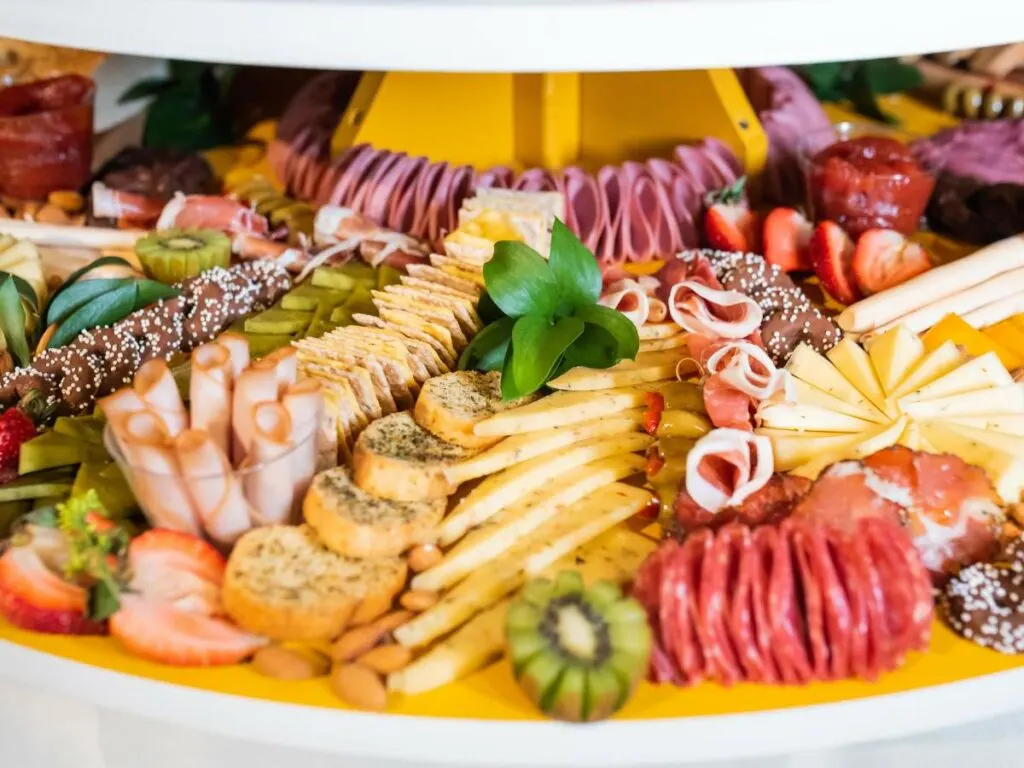 A colorful charcuterie board filled with various meats, cheeses, crackers, fruits, some garnishing leaves, and other assorted snacks.