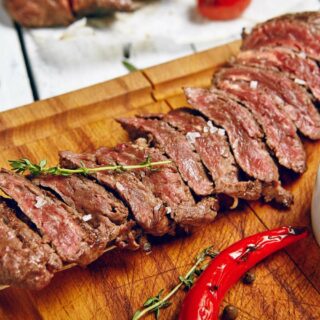 Sliced medium-rare steak on a wooden board, garnished with fresh thyme and a red chili pepper.