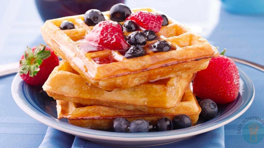 A plate of waffles topped with strawberries, blueberries, and a dollop of cream.