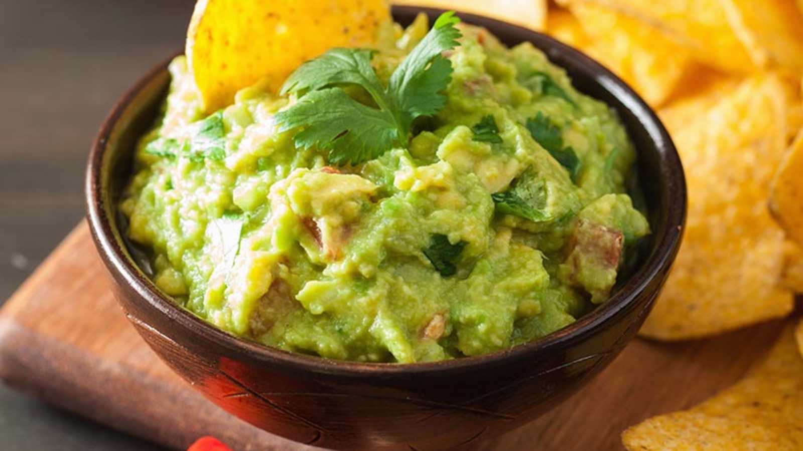 Two bowls of guacamole on tray with chips and various ingredients.