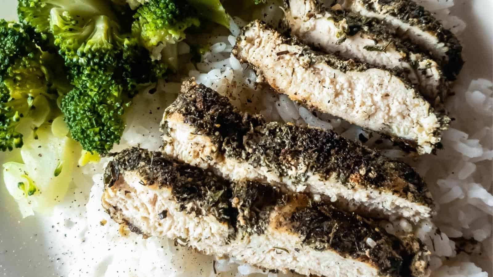 Sliced herb-crusted chicken breast served over white rice with a side of steamed broccoli.