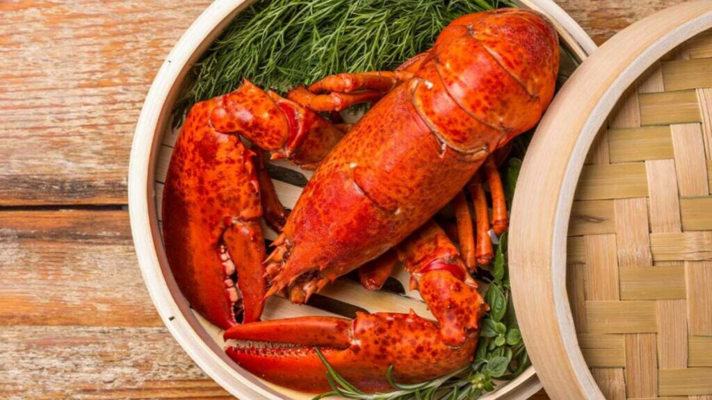 A cooked lobster is served in a wooden steamer basket with green garnishes around it.