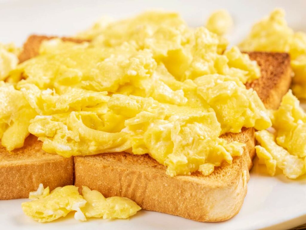 Close-up of scrambled eggs on top of toasted bread slices. The eggs are fluffy and yellow, covering the toast completely.