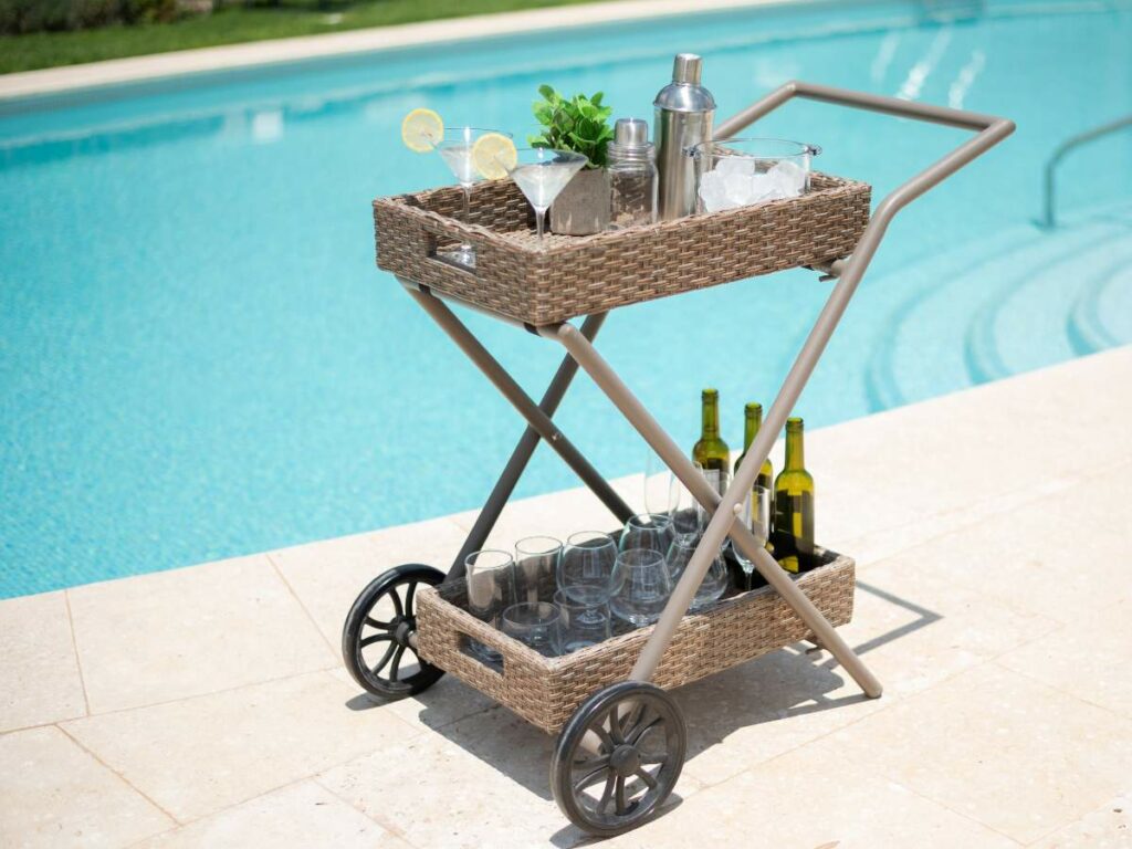 Wicker bar cart by a pool featuring a top tray with cocktail essentials and lemons.