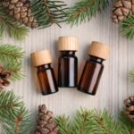 Three small amber bottles with wooden caps are placed in the center of a table, surrounded by pinecones and fir branches.