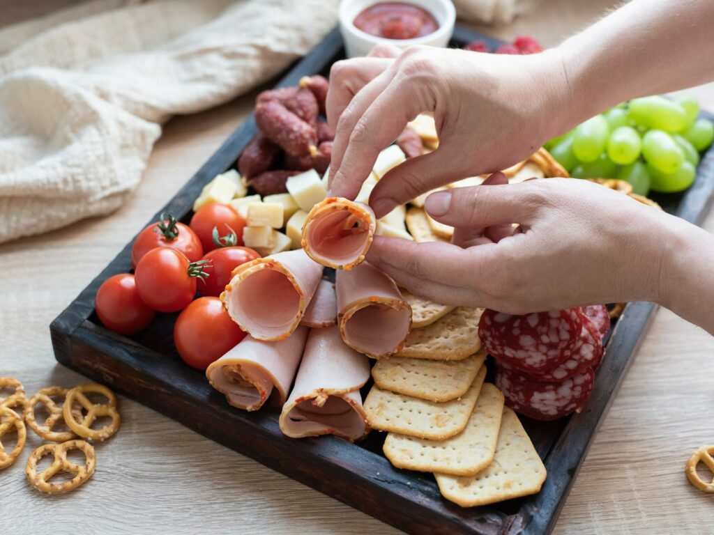 A charcuterie board being arranged by two hands.