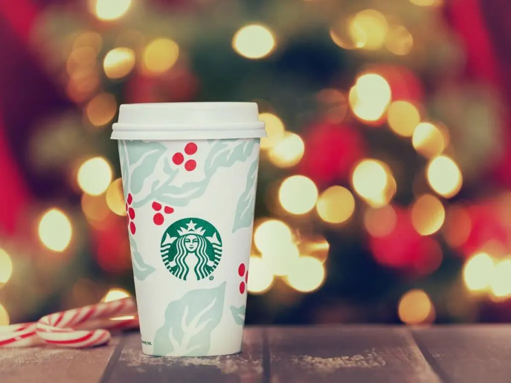 A Starbucks holiday-themed cup with a white lid is placed on a wooden surface.