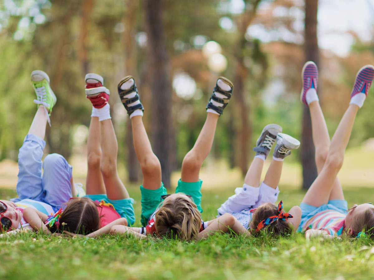 Five children lying on the grass with their legs raised in the air, wearing colorful clothes and shoes.