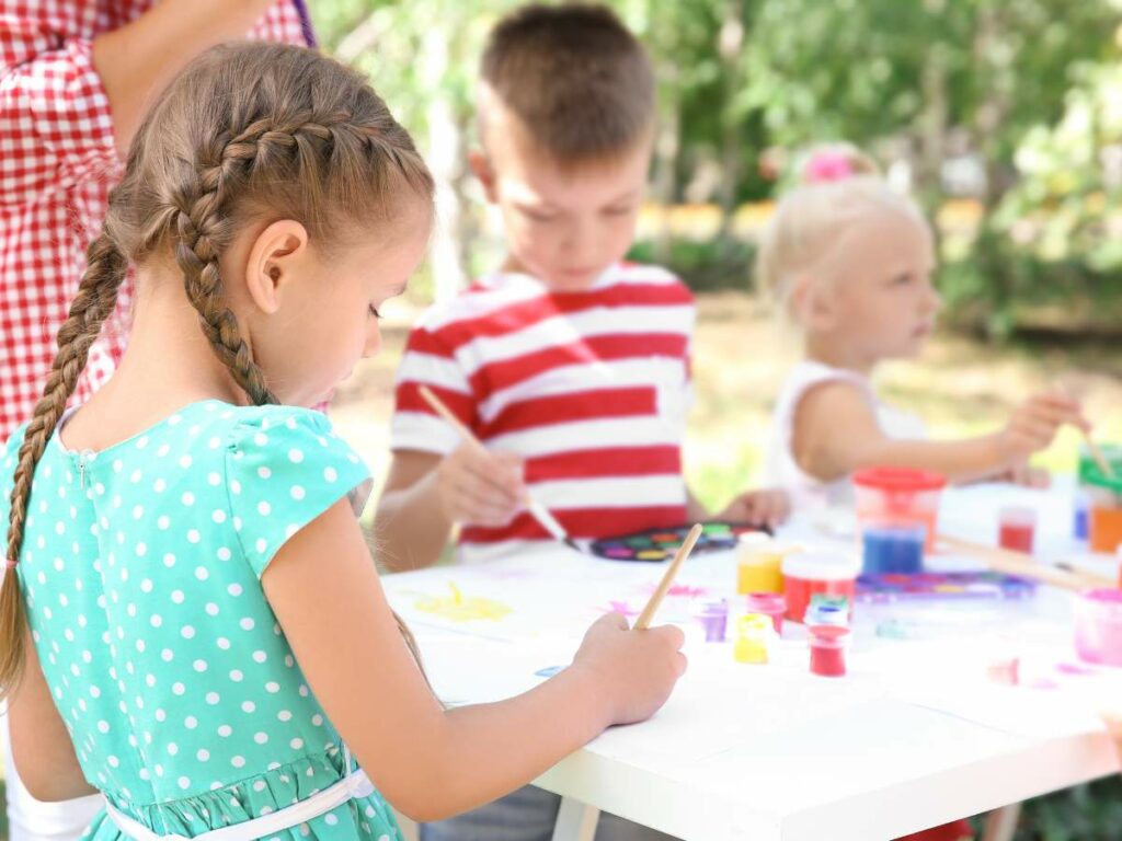 Three children painting at a table outdoors.